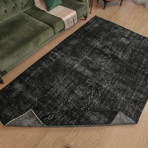 Pode incluir: Um tapete de &aacute;rea preto e branco com um visual desgastado e vintage. O tapete tem um padr&atilde;o sutil de linhas e redemoinhos brancos sobre um fundo preto.