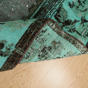 May include: Close-up of the edge of a teal and black patterned rug with a brown fringe. The rug is folded over and the underside is visible.