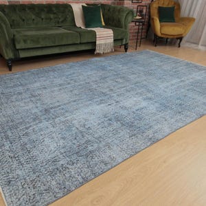 May include: A large rectangular area rug featuring a distressed, faded pattern in shades of light blue, slate grey, and white. The rug has a low-pile texture with a visible border design and a weathered, vintage-inspired appearance across the surface.
