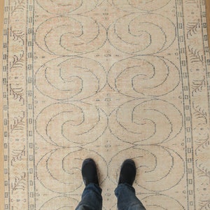 May include: A beige rug with a repeating pattern of swirls. The rug has a border with a floral design.