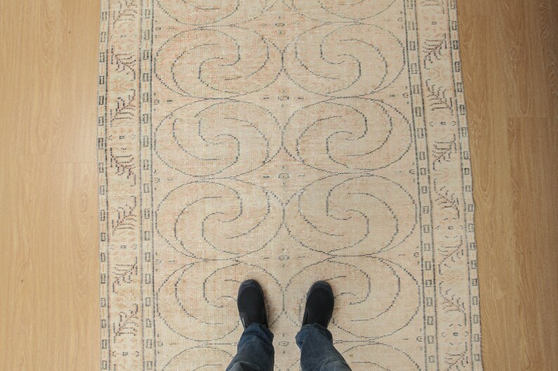 May include: A beige rug with a repeating pattern of swirls. The rug has a border with a floral design.