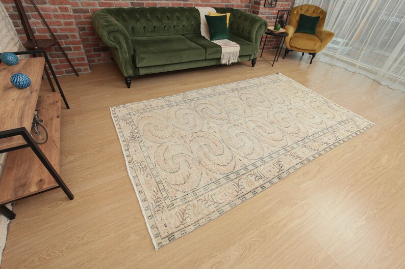 May include: A cream-colored rug with a geometric pattern of swirls and lines. The rug has a light brown border and is laid out on a wooden floor.