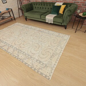 May include: A beige rug with a blue and white geometric pattern. The rug has a border with a repeating design. The rug is on a light wood floor.