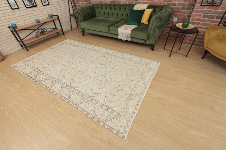 May include: A beige rug with a blue and white geometric pattern. The rug has a border with a repeating design. The rug is on a light wood floor.