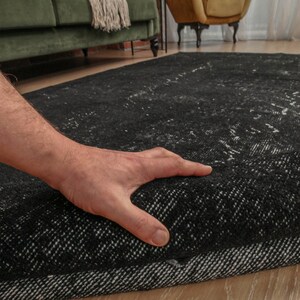 Pode incluir: Uma m&atilde;o estende-se para tocar um tapete com padr&otilde;es preto e branco. O tapete tem uma textura grossa e felpuda e um brilho sutil.