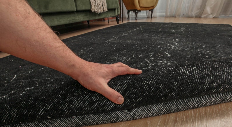 Pode incluir: Uma m&atilde;o estende-se para tocar um tapete com padr&otilde;es preto e branco. O tapete tem uma textura grossa e felpuda e um brilho sutil.
