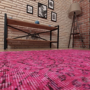 May include: A bright pink rug with an intricate design fills the lower portion of the image. The room features a brick wall, wooden shelving, and a floor lamp. The overall aesthetic suggests a warm and inviting space.