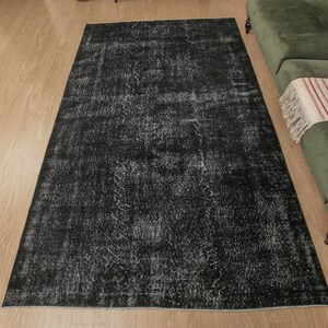 Pode incluir: Um tapete preto e branco desgastado com um visual vintage. O tapete tem uma apar&ecirc;ncia desbotada e desgastada, o que lhe confere um charme &uacute;nico e r&uacute;stico.