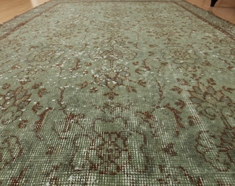 May include: A vintage green and brown rug with a floral pattern. The rug has a distressed look and is made of a soft, woven material.