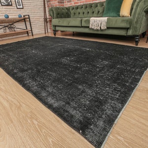 Pode incluir: Um tapete preto e branco desgastado com um padr&atilde;o sutil. O tapete est&aacute; colocado sobre um piso de madeira clara.