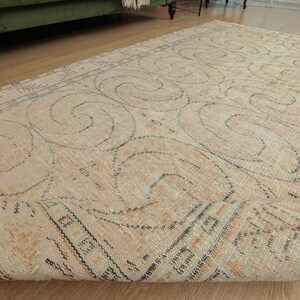 May include: A beige rug with a black and white geometric pattern. The rug has a distressed look and is rolled up.