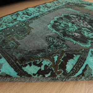 May include: A teal and black vintage rug with a floral pattern. The rug has a frayed edge and is made of a soft, woven material.