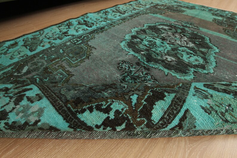 May include: A teal and black vintage rug with a floral pattern. The rug has a frayed edge and is made of a soft, woven material.