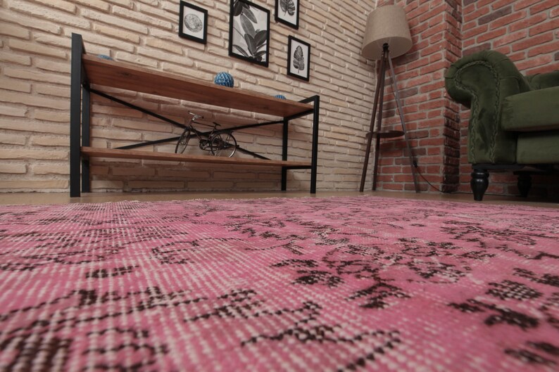 May include: A rectangular area rug featuring a vibrant pink base color with intricate, faded black floral and geometric patterns distributed across the surface. The rug has a low-pile texture and visible fringe detailing along the short edges.