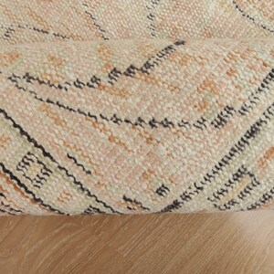 May include: Close-up of a rolled-up rug with a geometric pattern in shades of beige, brown, and black.