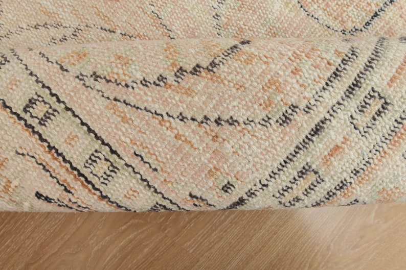 May include: Close-up of a rolled-up rug with a geometric pattern in shades of beige, brown, and black.