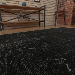 Pode incluir: Um tapete preto e branco desgastado com um padr&atilde;o sutil. O tapete est&aacute; colocado em um piso de madeira em uma sala com paredes de tijolo.