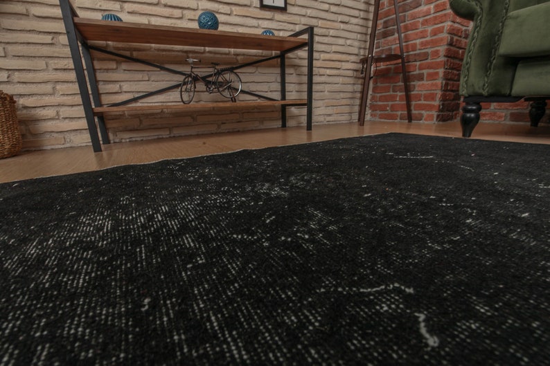 Pode incluir: Um tapete preto e branco desgastado com um padr&atilde;o sutil. O tapete est&aacute; colocado em um piso de madeira em uma sala com paredes de tijolo.