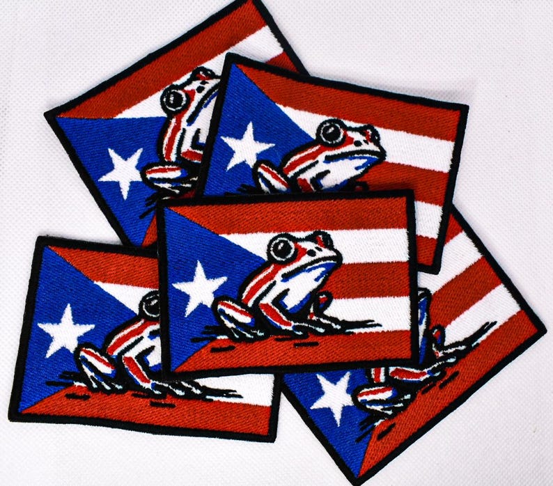May include: A collection of embroidered patches featuring the Puerto Rican flag design. Each patch has a blue triangle with a white star, red and white stripes, and a frog illustration. The patches have a black border.