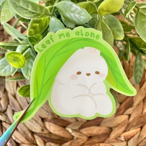 May include: A white cartoon character with a leaf covering its head. The leaf is green and has the text "Leaf me alone" written on it.