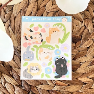 May include: A sheet of stickers featuring cute cartoon cats with different colored fur and floral designs. The stickers are on a white background with the text "pocketbun shop" at the top.