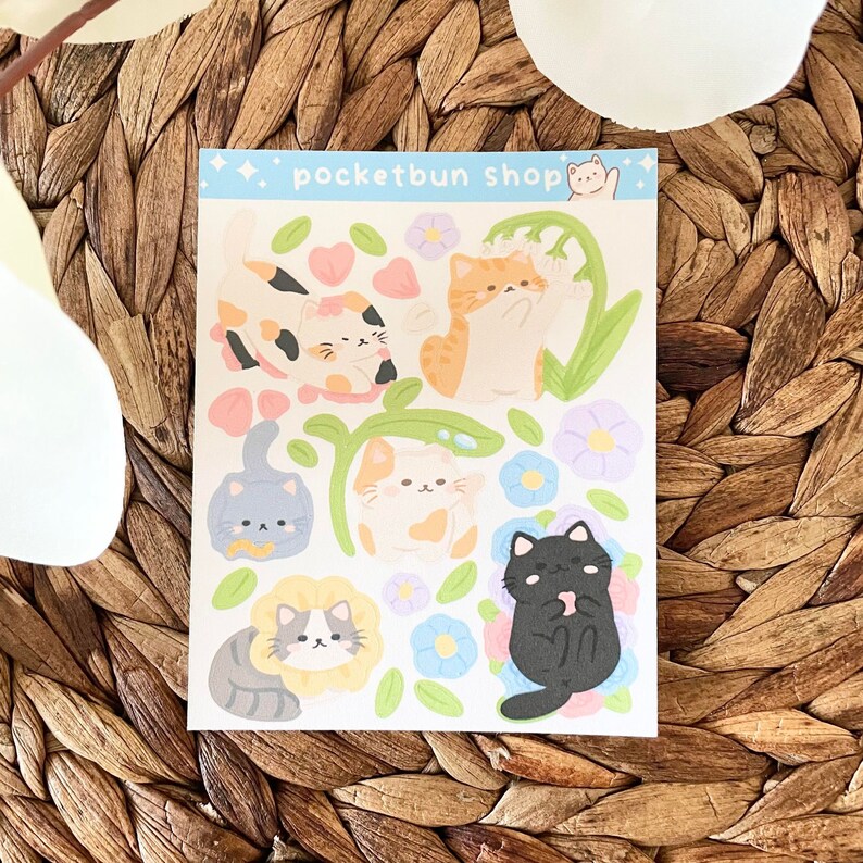 May include: A sheet of stickers featuring cute cartoon cats with different colored fur and floral designs. The stickers are on a white background with the text "pocketbun shop" at the top.