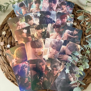 May include: A collection of rectangular trading cards featuring various anime-style male characters with diverse hair colors and expressions, arranged in an overlapping fan pattern on a woven circular mat with small white star-shaped accents.