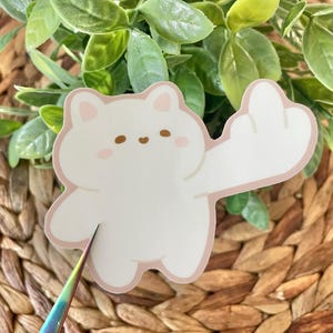 May include: White sticker of a cartoon bear with a pink blush on its cheeks giving the middle finger. The bear is outlined in a light pink color.