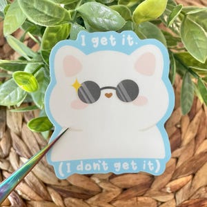 May include: A white cat wearing sunglasses with a blue background and the text "I get it. (I don't get it)"