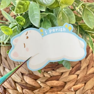 May include: White sticker with a cartoon white bear lying down with its eyes closed. The sticker has a blue outline and the text "I perish" in yellow with two yellow stars.
