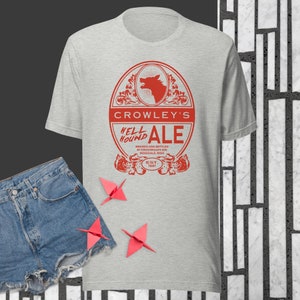 May include: A gray t-shirt with a red graphic of a beer label that says "Crowley's Hell Hound Ale" and "Brewed and Bottled by Crowley's Hell Hound Rosedale, Miss. Est. 1661".