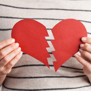 May include: A person is holding a red paper heart that is broken in half.