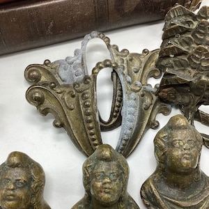 May include: A set of four antique brass drawer pulls. Two of the pulls feature ornate designs with a raised center, while the other two feature a more simple design with a raised face. The pulls are in good condition with some signs of wear and tear.