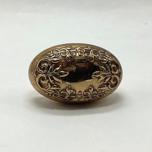 May include: A gold oval-shaped decorative knob with an intricate floral design.