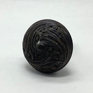 May include: A dark brown, round door knob with a detailed, swirling, carved design.