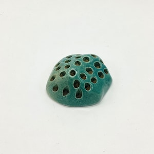 May include: A teal ceramic planter with a unique honeycomb design. The planter has many small holes throughout the surface.