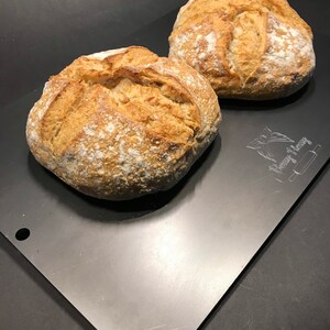 K&ouml;nnte beinhalten: Zwei frisch gebackene Sauerteigbrote auf einem silbernen Backblech. Das Brot ist goldbraun und hat eine leicht knusprige Kruste.