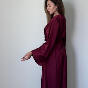 May include: A long, burgundy-coloured robe with wide sleeves. The robe is made of a soft, flowing fabric and is tied at the waist with a matching belt. The model is wearing the robe.