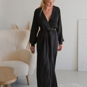 May include: A black satin robe with a V-neckline and a tie belt. The robe has long sleeves and a flowing silhouette.