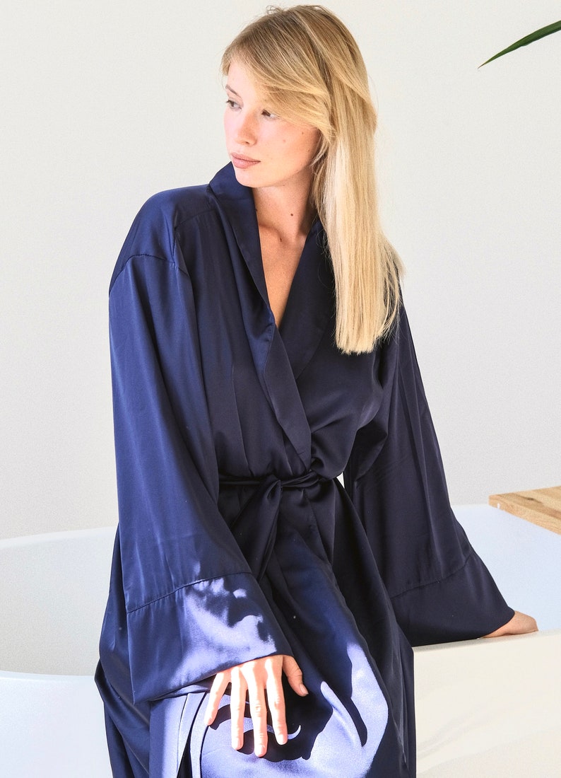 May include: A navy blue satin robe with long sleeves and a tie belt. The robe is open in the front, revealing the neckline.