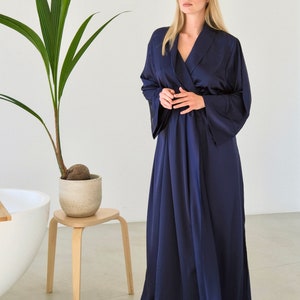 May include: A long, navy blue satin robe with a shawl collar and long sleeves. The robe is tied at the waist with a sash.