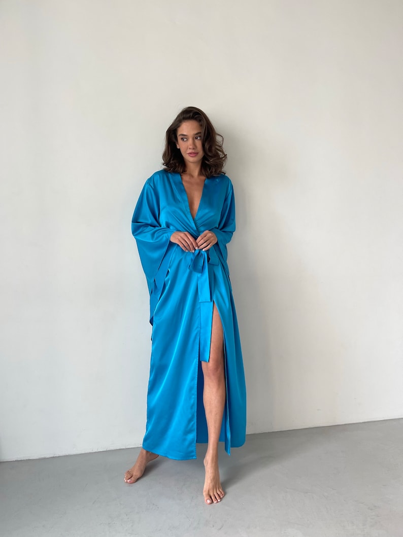 May include: A long, flowing blue satin robe with a tie belt and a side slit. The robe has wide, flowing sleeves.