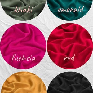 May include: Circular fabric swatches in khaki, emerald, fuchsia, red, gold, and black. Each swatch has a different color and a handwritten label. The fabric is gathered, showing its texture.