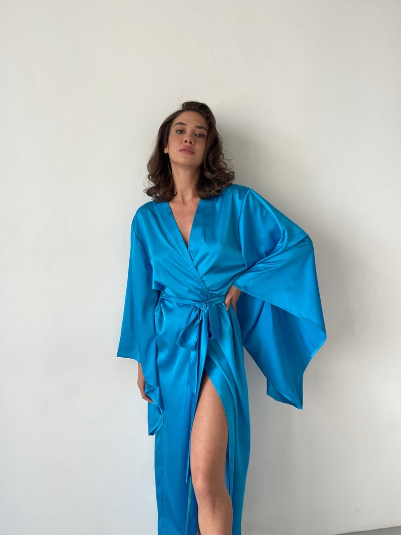 May include: A long, flowing blue satin robe with wide sleeves and a tie belt. The robe is open in the front, revealing a glimpse of the wearer's leg.
