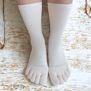 May include: A pair of off-white toe socks, designed to separate each toe. The socks have a ribbed cuff and a smooth, solid color design. The socks are made of a soft material and are suitable for casual wear.