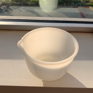 May include: A white ceramic mixing bowl with a smooth, rounded surface. The bowl is empty and has a slight lip around the top edge.