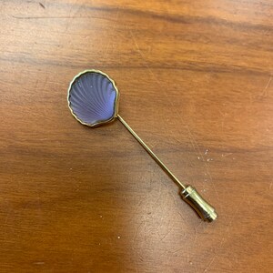 May include: A gold-toned pin with a purple glass seashell design.