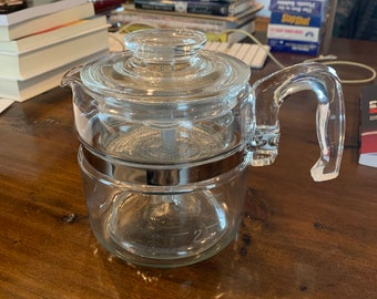 Op de afbeelding: Een glazen koffiekan met een zilveren band rond het midden. De kan heeft een glazen deksel en een glazen handvat.