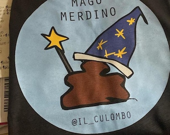 Pode incluir: Camiseta preta com um design de desenho animado engraçado. O design apresenta uma figura marrom em forma de cocô usando um chapéu de mago azul com estrelas amarelas, segurando uma varinha de estrela amarela. O texto "MAGO MERDINO" está acima.