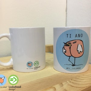 Può includere: Una tazza in ceramica bianca con sfondo blu e un uccello dei cartoni animati con corpo rosa e becco giallo. Il testo "TI ANO" è sopra l'uccello e "@IL_CULOMBO" è sotto l'uccello. Il retro della tazza ha un piccolo uccello dei cartoni animati con corpo rosa e becco giallo e il testo "Lookahead design" in nero.